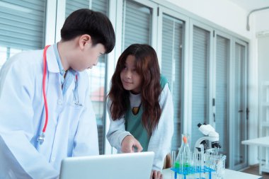 Fen sınıfında, Asyalı bir çocuk bilim adamı kimyasal formüller üzerinde deney yapıyor.