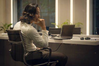 Side view of young businessman sitting at desk in office and looking away, Business disappointment concept clipart