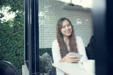 Kafede akıllı telefon kullanan Asyalı güzel bir kadının portresi.