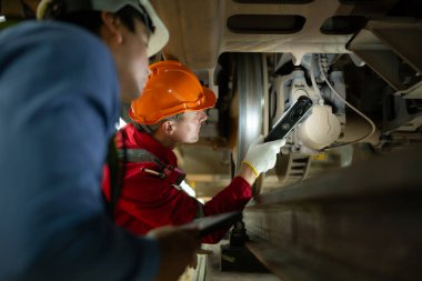 Elektrikli trenler için iki mühendis, elektrikli trenin mekanizmalarında sorun tespit ettikten sonra hasar gören bölümleri tespit etmek ve kontrol etmek için projektörleri kullanır. Elektrikli tren tamirhanesinde.