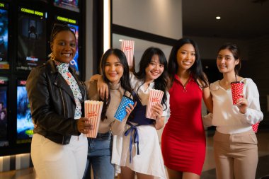 Group of happy friends watching movie in cinema and eating popcorn at night clipart