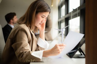 Genç iş kadını ve çeşitli iş adamları ofiste birlikte çalışarak rüzgar ve güneş ışığından elde edilen doğal enerjinin müşterilere nasıl sunulacağı konusunda beyin fırtınası yapıyorlar..