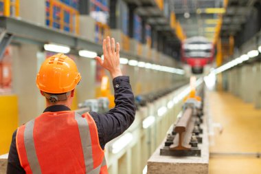 Güvenlik kaskı ve yansıtıcı yelek giyen elektrikli tren mühendisinin arka görüntüsü. Araba tamir fabrikasında arka plan olarak elektrikli bir araba var..