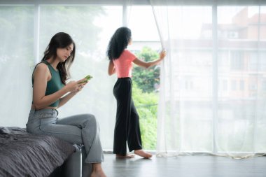 Genç bir kadın evdeki oturma odasında uzlaşmak için can atan bir arkadaşıyla akıllı telefon kullanıyor, aşk kavramı LGBT