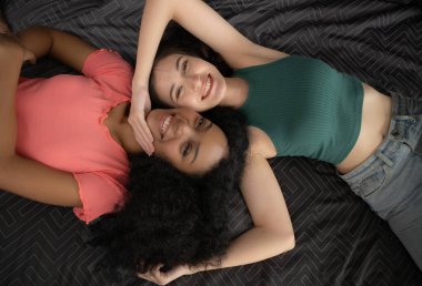 Top view of two young women lying on bed and smiling at each other clipart