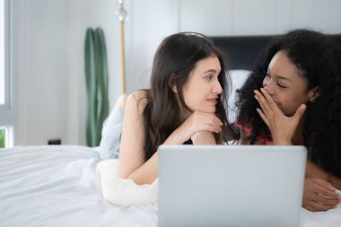 Evde dizüstü bilgisayar kullanan mutlu lezbiyen çift. Yatak odasında dizüstü bilgisayar kullanan çok ırklı genç lezbiyen çift. Teknoloji ve aşk kavramı