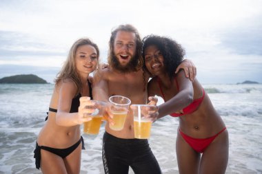 Çok ırklı arkadaş grubu sahilde eğleniyor, bira içiyor ve eğleniyorlar.
