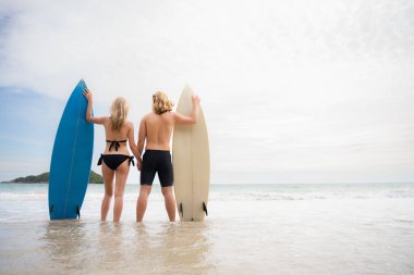 Sahilde sörf tahtası olan, mayolu genç bir adam ve kadın..