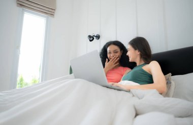 Evde dizüstü bilgisayar kullanan mutlu lezbiyen çift. Yatak odasında dizüstü bilgisayar kullanan çok ırklı genç lezbiyen çift. Teknoloji ve aşk kavramı