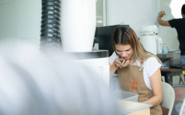 Önlüklü genç kadın dijital tablet kullanarak kahve çekirdeklerinin kalitesini kontrol ediyor.