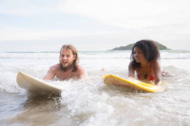Genç adam ve kadın güneşli bir günde okyanusta sörf tahtası ile eğleniyorlar.
