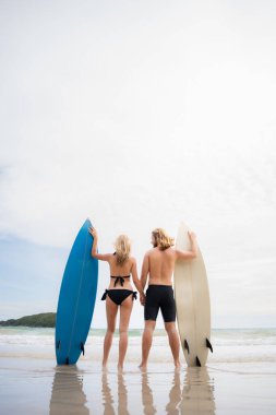 Sahilde sörf tahtası olan, mayolu genç bir adam ve kadın..