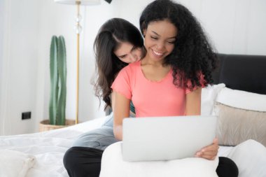 Evde dizüstü bilgisayar kullanan mutlu lezbiyen çift. Yatak odasında dizüstü bilgisayar kullanan çok ırklı genç lezbiyen çift. Teknoloji ve aşk kavramı