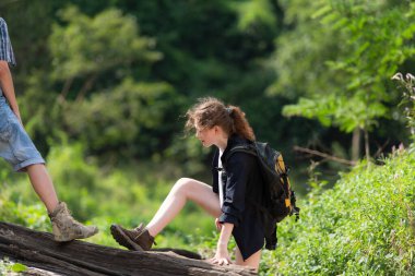 Sırt çantalı genç bir kadın ormanda bir kütüğe tırmanıyor..