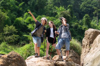 Sırt çantalı bir grup turist nehirde ve dağlarda yürüyor.