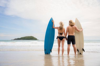 Sahilde sörf tahtası olan, mayolu genç bir adam ve kadın..