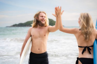 Sahilde iki sörfçü beşlik çakıyor. İki sörfçü sahilde eğleniyor..