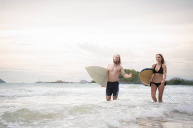 Sörf tahtalarını tutan genç adam ve kadın sörf yapmak için denize girmeye hazırlar..