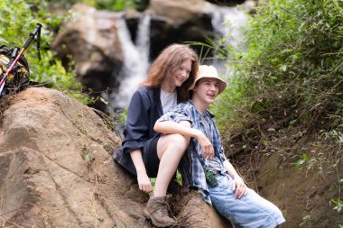 Bir kayanın üzerinde oturmuş öpüşen iki genç yürüyüşçü.