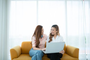 LGBT çifti koltukta oturuyor ve evde dizüstü bilgisayar kullanıyorlar..