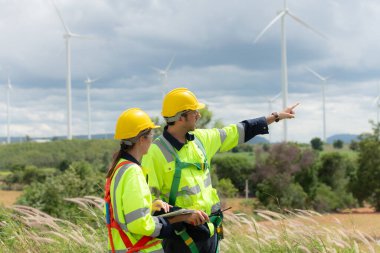 Mühendis ve işçi rüzgar türbinlerinin arka planında projeyi tartışıyor