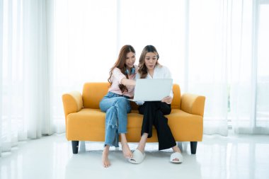 LGBT çifti koltukta oturuyor ve evde dizüstü bilgisayar kullanıyorlar..