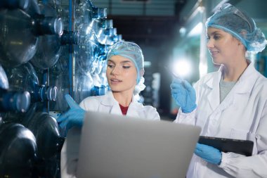 İki genç kadın bilim adamı içme suyu fabrikasında tablet bilgisayarla çalışıyor.