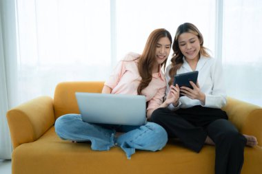 LGBT çifti koltukta oturuyor ve evde dizüstü bilgisayar kullanıyorlar..