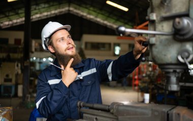 Makine mühendislerinin portresi, bir süredir kullanılan eski bir makinenin çalışma koşullarını kontrol ediyor. Doğal ışığın işyerinde parladığı bir fabrikada.