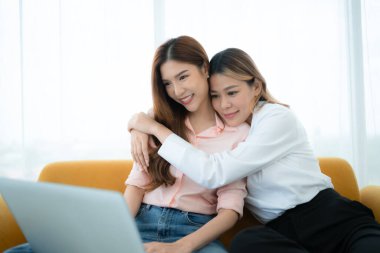 LGBT çifti koltukta oturuyor ve evde dizüstü bilgisayar kullanıyorlar..