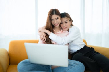 LGBT çifti koltukta oturuyor ve evde dizüstü bilgisayar kullanıyorlar..