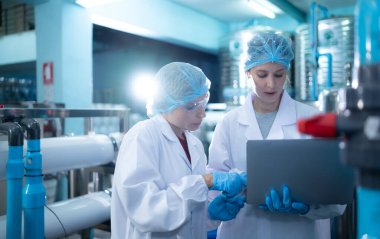 İki genç kadın bilim adamı içme suyu fabrikasında tablet bilgisayarla çalışıyor.