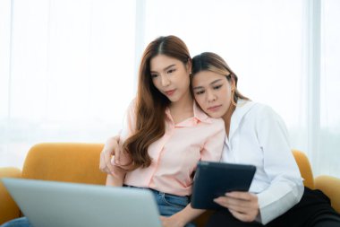 LGBT çifti koltukta oturuyor ve evde dizüstü bilgisayar kullanıyorlar..