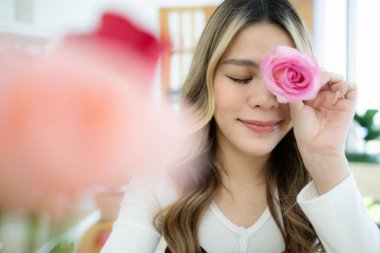 Elinde pembe bir çiçek tutan gülümseyen Asyalı kadın.