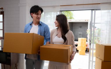 Genç Asyalı çift yeni evlerinde kutu taşıyor. Ayaktalar ve gülümsüyorlar..