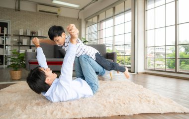 Bir çocuk, babasının yerden yükseklere uçmasına yardım etmek için bacaklarını kullanarak uçmak ister. Oturma odasında.