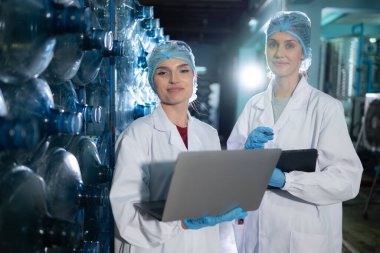 İki genç kadın bilim adamı içme suyu fabrikasında tablet bilgisayarla çalışıyor.