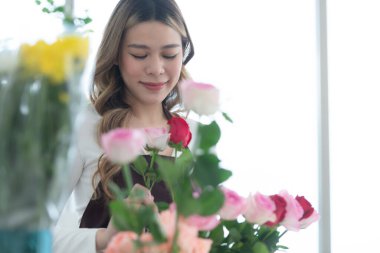 Çiçekçide kırmızı gül kokusu alan genç bir kadın.