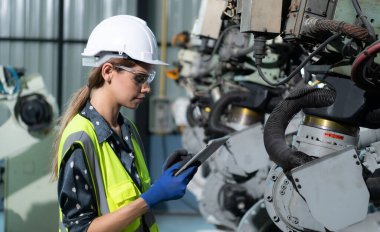 Kadın bir mühendis robot deposundaki robot koluna bir program yüklüyor. Makineyi müşteriye göndermeden önce işlemi test edin.