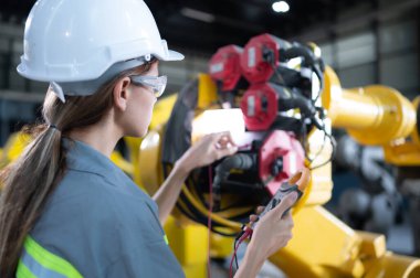 In the robots warehouse, A female engineer inspects the electrical system of every robotics arm, before delivering to the customer. clipart