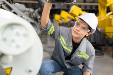 Kadın bir mühendis robot deposundaki robot koluna bir program yüklüyor. Makineyi müşteriye göndermeden önce işlemi test edin.