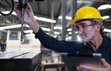 Yaşlı bir teknisyen, çelik yumruk makinesinin işletim kontrolünü test etmek için bilgisayar kullanıyor..