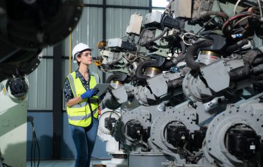 Kadın bir mühendis robot deposundaki robot koluna bir program yüklüyor. Makineyi müşteriye göndermeden önce işlemi test edin.