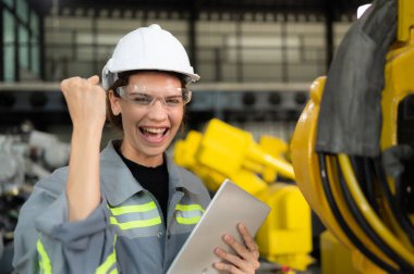 In the robots warehouse, Female engineer happily with updating software and calibrating a robotics arm. clipart