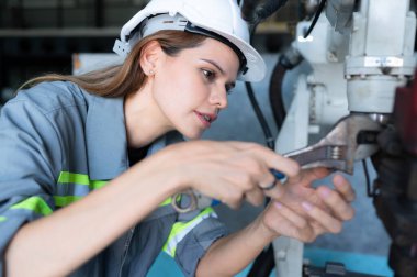 Robot hangarında robotik kolu denetleyen ve onaran kadın teknisyen bir süre kullanıldıktan sonra makinenin işleyişini test ediyor, ayrıca yazılım ve kalibrasyonu güncelliyor.