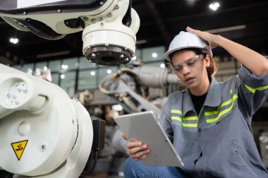 Kadın bir mühendis robot deposundaki robot koluna bir program yüklüyor. Makineyi müşteriye göndermeden önce işlemi test edin.