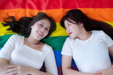 Gökkuşağı bayrağında, bir LGBT çifti mutlu bir şekilde uzanıp sohbet ediyor ve birbirlerine sataşıyorlar..