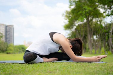Şehir parkında açık hava aktiviteleri yapan genç bir kadın. Yoga onun seçtiği bir aktivite..