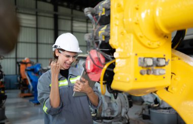 In the robots warehouse, Female engineer happily with updating software and calibrating a robotics arm. clipart