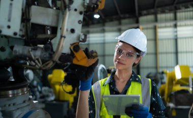Kadın bir mühendis robot deposundaki robot koluna bir program yüklüyor. Makineyi müşteriye göndermeden önce işlemi test edin.